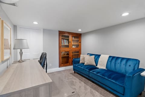 A cozy room with a blue velvet sofa, desk, lamp, and bookshelf.