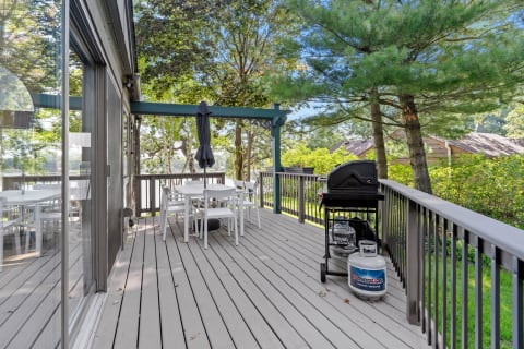 Outdoor deck with a dining table, chairs, and a grill, set among trees and greenery.