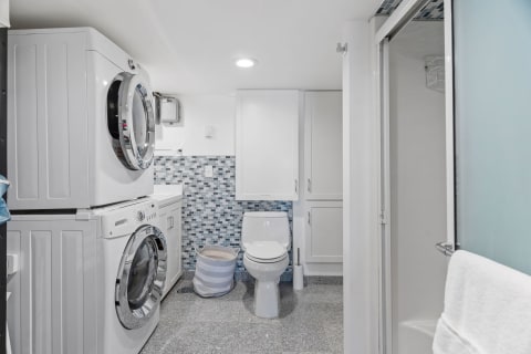 A compact laundry and bathroom area with a washing machine, dryer, toilet, and a shower door.