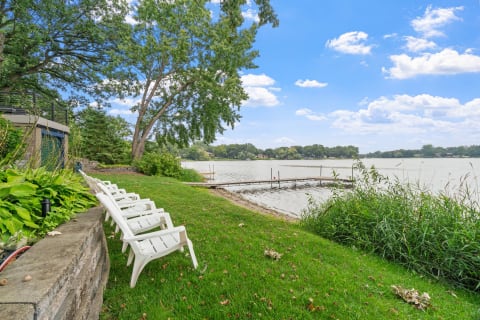 Lakeside scene featuring a lawn with white chairs and a dock on the water.