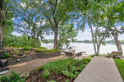 Lakeside landscape with greenery, a brick pathway, and seating area overlooking the water.