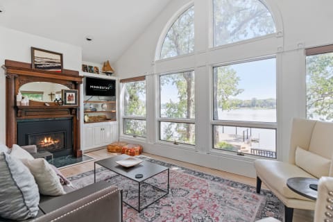 Living room with fireplace overlooking a lake through large arched windows.