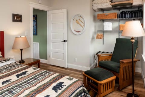 A bedroom featuring a bed with a patterned quilt, a green armchair, and organized shelves.