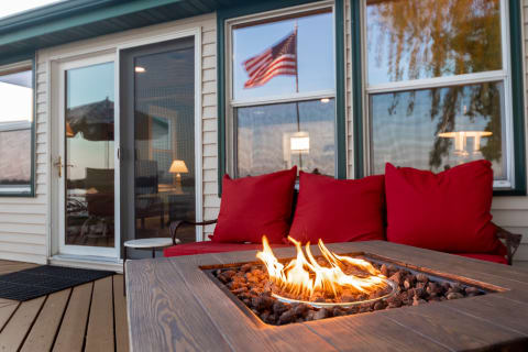 Outdoor seating area with a fire pit and red cushions in front of a house with an American flag.