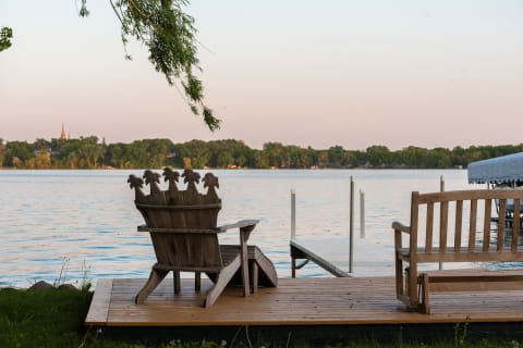 Lakeside scene with wooden chairs on a deck overlooking calm waters.