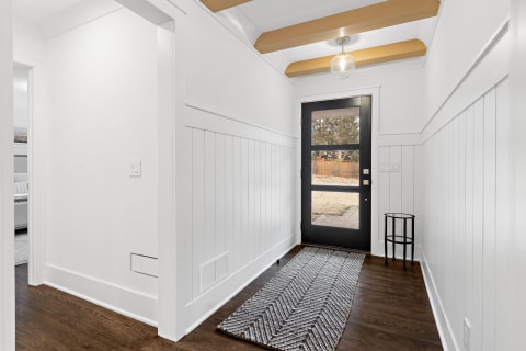 Bright and modern entryway with black front door and white wainscoting.