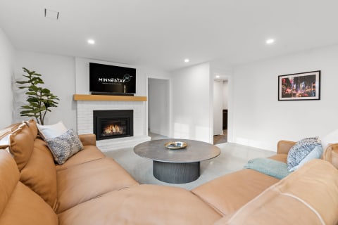 A modern living room featuring a leather sectional couch, a round coffee table, and a white brick fireplace with a TV above it.