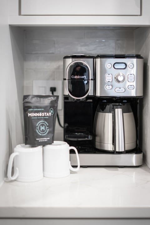 Modern Cuisinart coffee maker with coffee bags and white mugs on a marble countertop