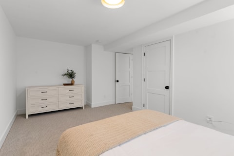 Interior view of a minimalistic bedroom with a dresser and bed.