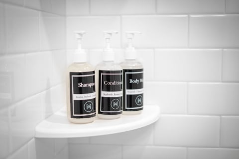 Three personal care bottles on a shower shelf labeled shampoo, conditioner, and body wash.