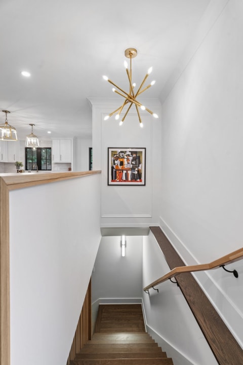 Modern staircase with a gold chandelier and colorful artwork on the wall.