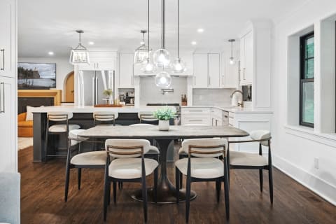 Modern kitchen and dining area showcasing a round table, upholstered chairs, and white cabinetry.