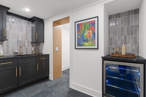 Modern kitchen featuring black cabinets, gray tile backsplash, and colorful artwork.