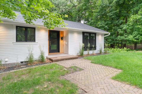 Modern home with a wooden entrance and black windows, surrounded by trees and grass.