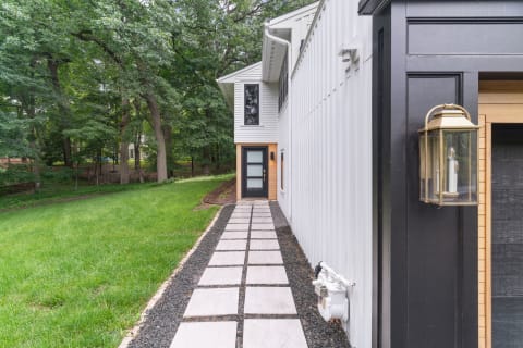 Pathway beside a contemporary home with a black door and surrounding trees.