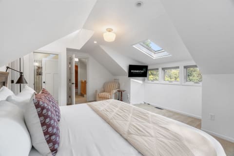 Attic bedroom with a bed, skylight, windows, and TV.