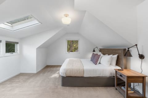 A modern attic bedroom with sloping ceilings, a bed, and a wooden bedside table.