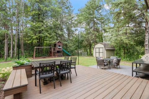 Backyard with a dining set, playground, and a shed surrounded by trees.