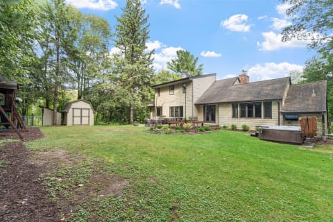 Backyard view of a two-story house surrounded by trees and a play structure.