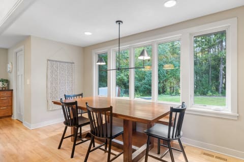 A bright dining area featuring a wooden table, black chairs, and large windows overlooking greenery.