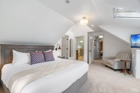 An attic bedroom with a king-sized bed, reading lamp, seating area, and a modern bathroom entrance.
