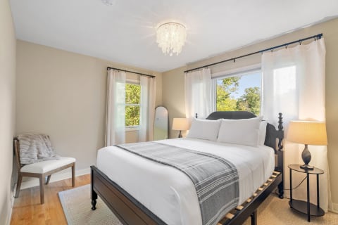 A serene bedroom with a black bed frame, white bedding, and sheer curtains, illuminated by natural light.