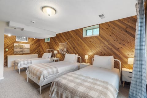 Cozy bedroom featuring three beds, wooden paneled walls, and simple decor.