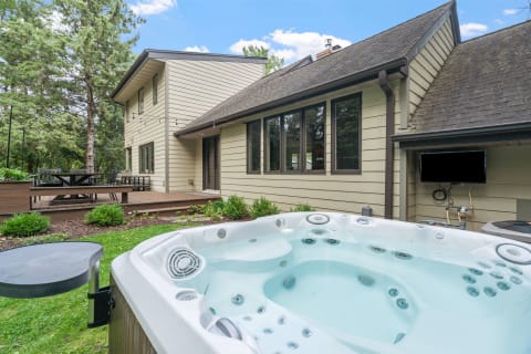 Backyard featuring a hot tub, a wooden deck with outdoor seating, and a beautiful house.
