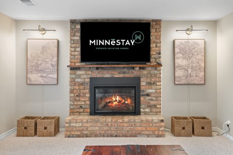 A stylish living room with a brick fireplace, modern TV displaying a logo, and framed artwork.