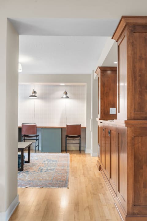 Interior view showing wooden cabinetry, chairs, and a patterned rug in a living area.