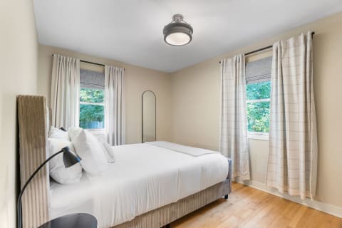 A serene bedroom with a queen-size bed, beige walls, and light wooden flooring.