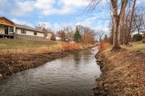 A peaceful creek flows through a tranquil neighborhood, framed by trees and modern homes.