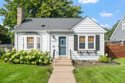 A charming single-story home with a blue exterior and beautiful flower beds.