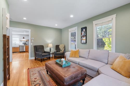 A cozy living room featuring a sectional sofa, leather ottoman, and a modern kitchen view.