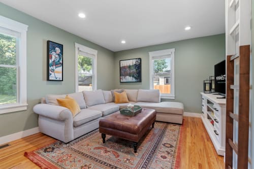 A cozy living room with a sectional sofa, leather ottoman, and vibrant artworks.
