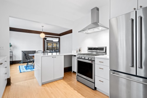 A modern kitchen featuring sleek white cabinetry and stainless steel appliances, highlighted by warm wooden floors.