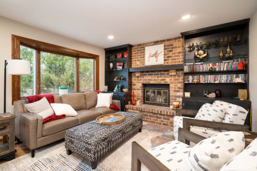 A cozy and stylish living room featuring a leather sofa, patterned ottoman, and a brick fireplace.
