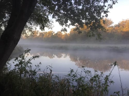 A serene river at dawn, surrounded by mist and autumn foliage.
