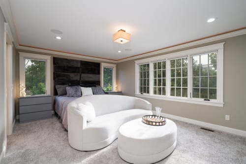 A modern and serene bedroom featuring a stylish bed, loveseat, and large windows.