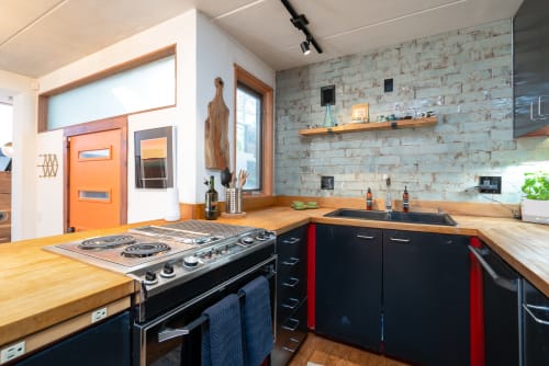 A modern kitchen blending rustic and contemporary design with an orange door.