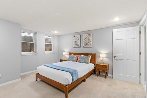 A cozy bedroom with a warm wooden bed, decorative prints, and bright lighting.