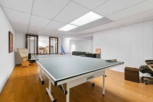 A spacious basement recreation room with a ping pong table and cozy seating.