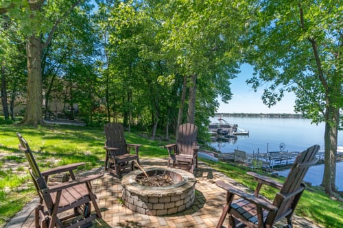 A tranquil lakeside setting with Adirondack chairs around a fire pit.