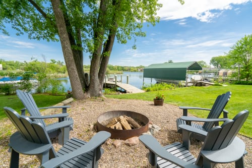A tranquil lakeside gathering spot featuring a fire pit and Adirondack chairs.