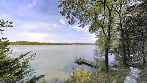 A tranquil lakeside view featuring a wooden dock and lush greenery.