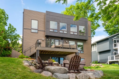 Modern house with a spacious deck and Adirondack chairs in the backyard.
