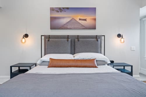 A modern and tranquil bedroom featuring a grey upholstered headboard, sunset lake photography, and ambient lighting.
