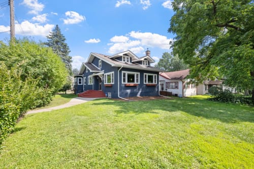 A charming blue two-story house with a welcoming front porch and lush greenery.