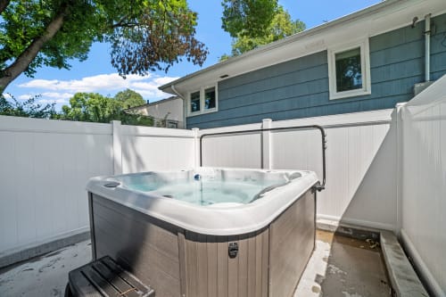 A tranquil backyard hot tub scene surrounded by a privacy fence and greenery.