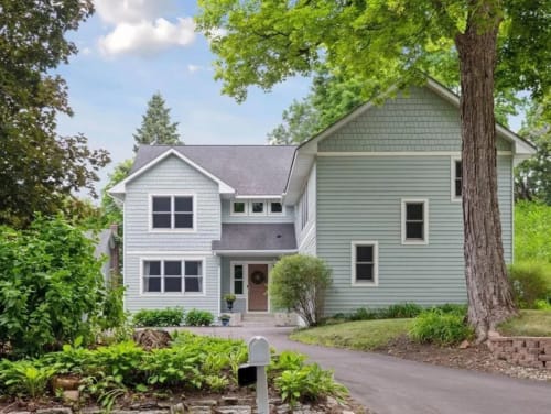A charming two-story light blue house surrounded by greenery.
